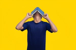 Stressed student covering face with book due to exam pressure and poor preparation.