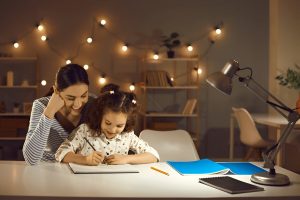Parent helping child study at home with books and laptop, creating a positive learning environment